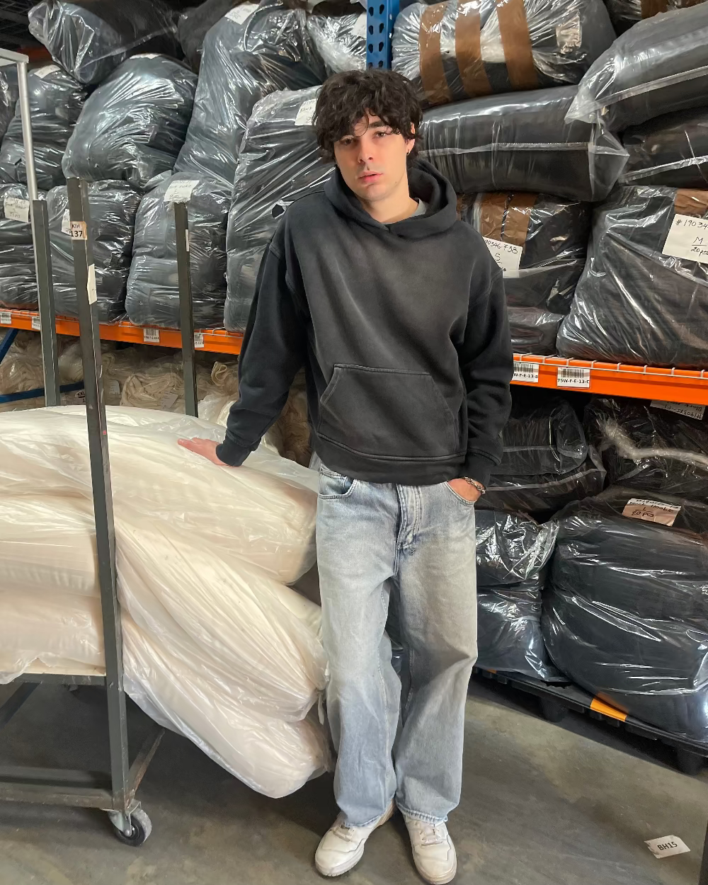 Person standing in a warehouse with stacked materials and plastic wrap.
